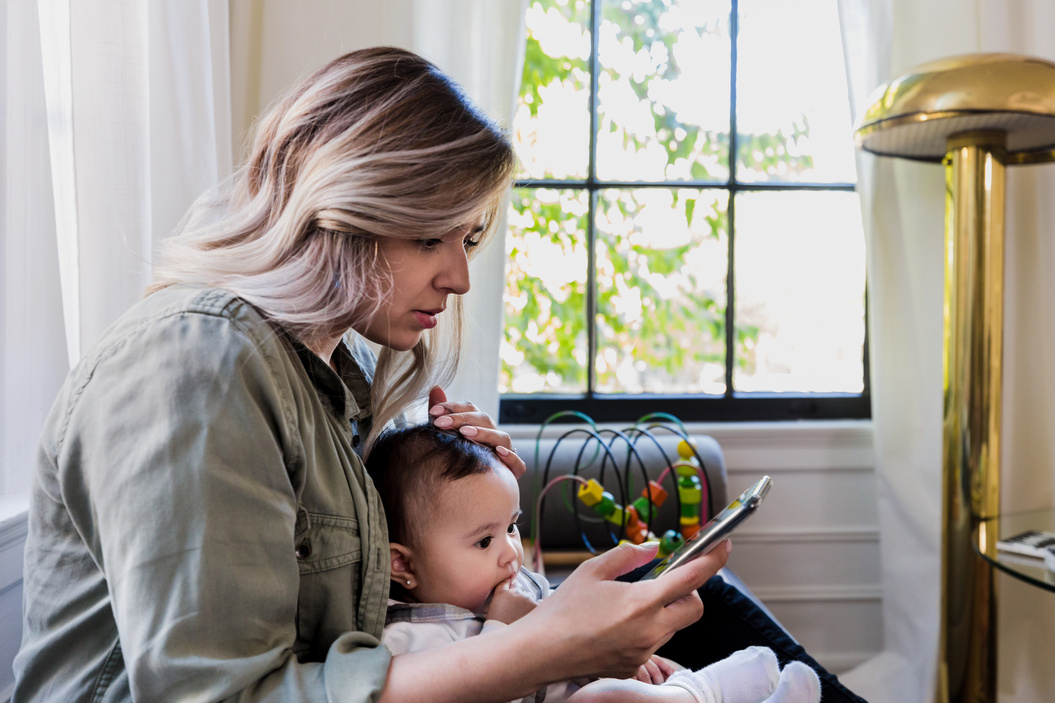 Worried mom with sick baby scrolls through information on phone